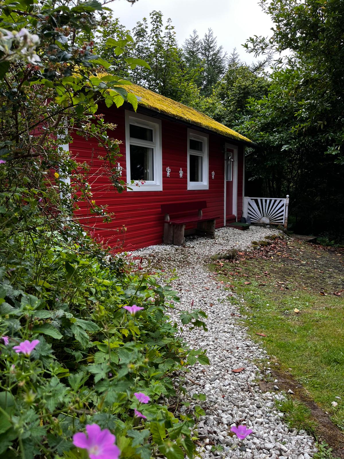 The red cottage in its garden, with flowers and a gravel path