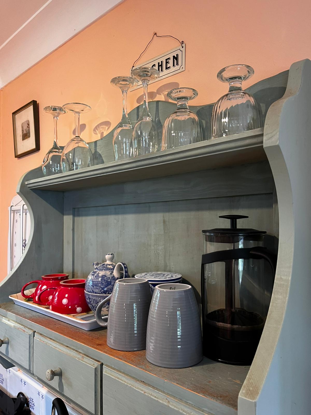 Green kitchen dresser with cups, a teapot, coffee pot and glasses